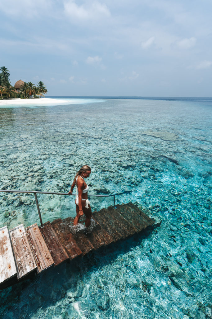Woman walking down stairs into the water to swim among the corals.