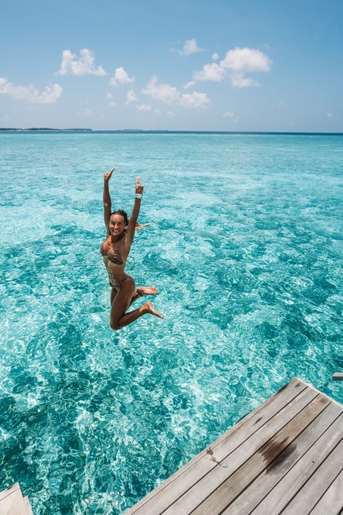 Woman jumping into turquoise water from a timber jetty