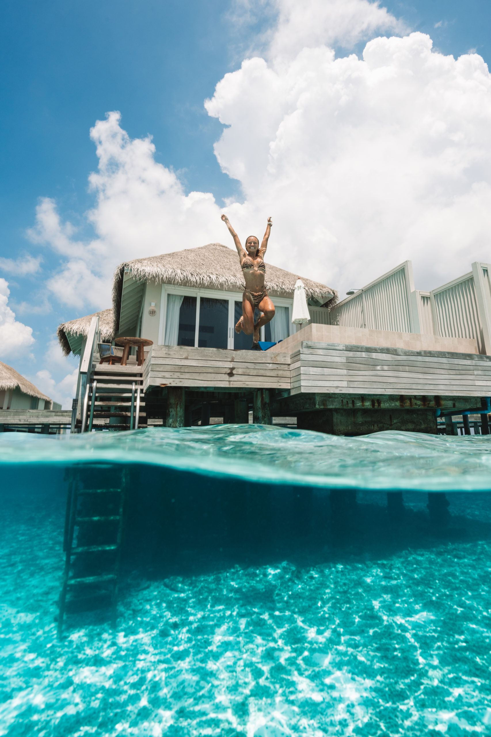 Salty Luxe jumping off of the deck of one of the Maldives overwater bungalows at baglioni