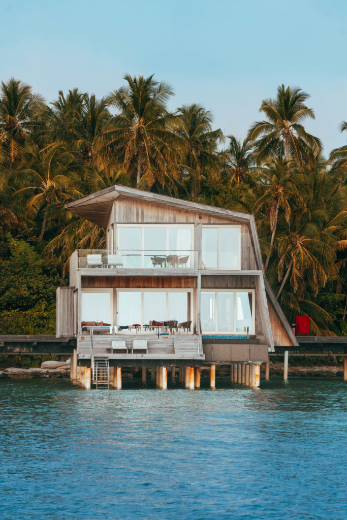 Two storey beach villa, set over the water with palm trees surrounding.