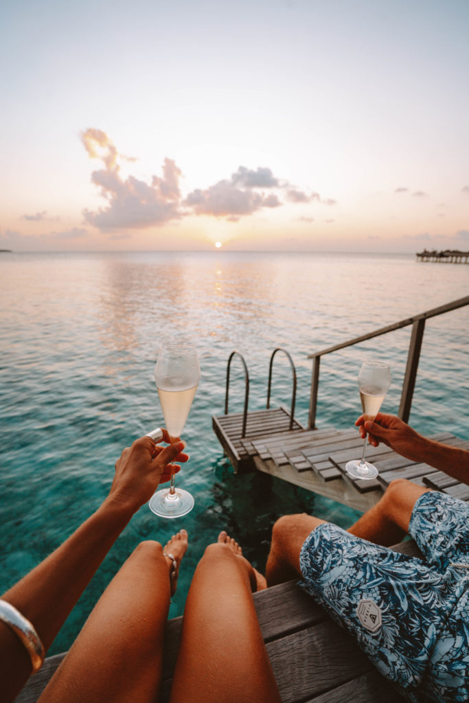 Couple holding flutes of champagne and watching the sunset.
