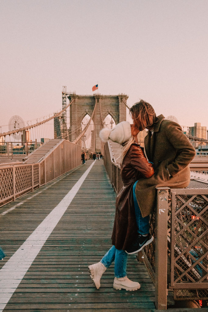 Couple kissing on Brooklyn Bridge at sunset.