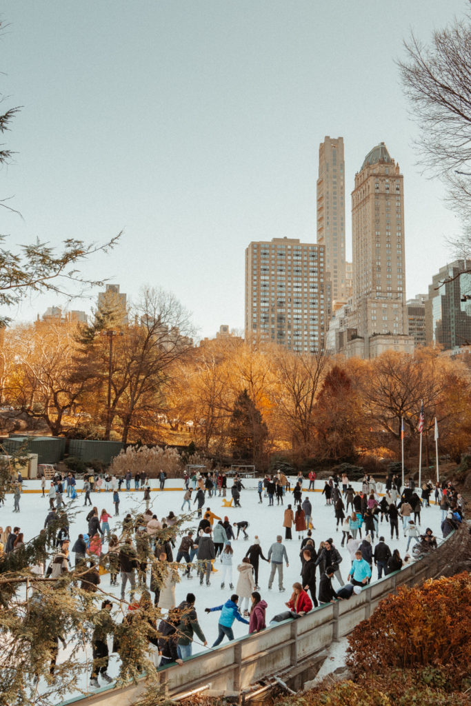 A large crowd ice skates in a winter wonderland in Central Park.