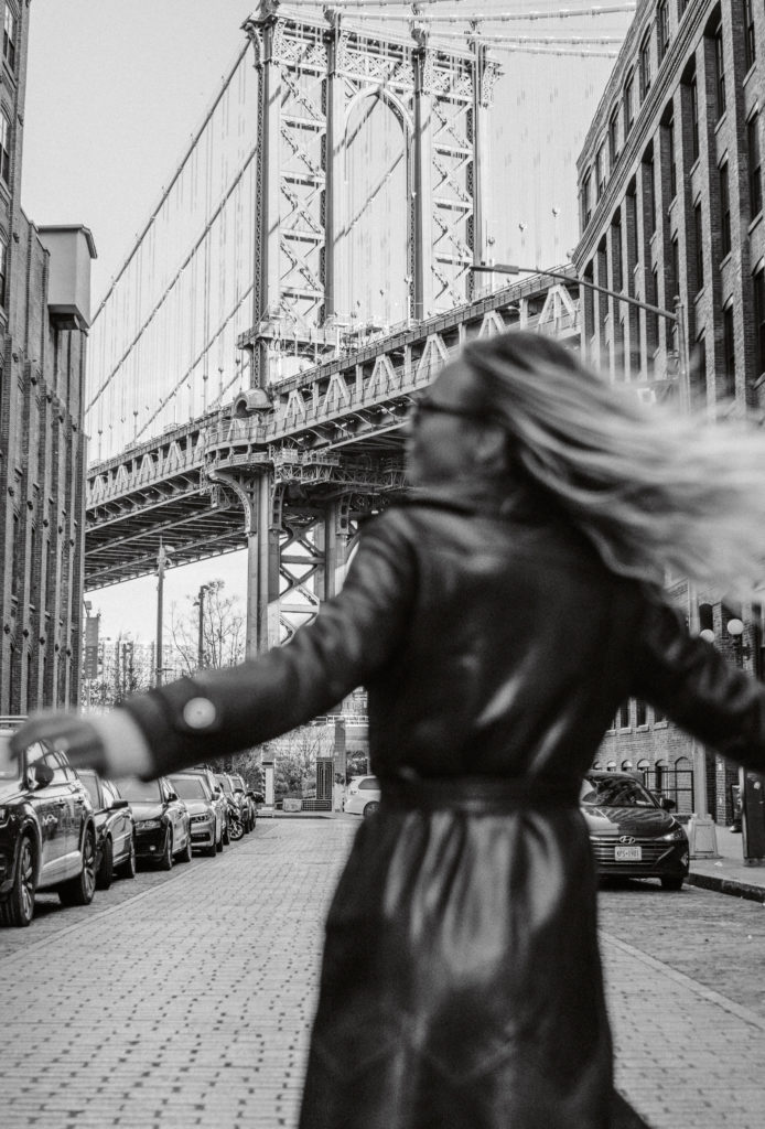 Black & white images of woman dancing in the street in Dumbo, with the Brooklyn bridge in the background on an iconic street.