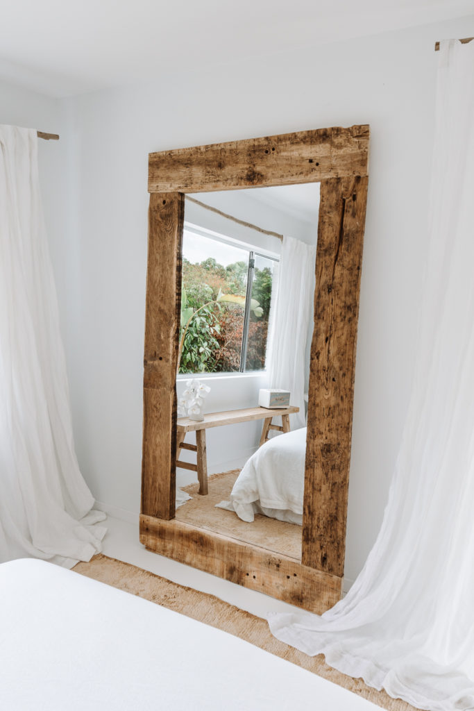 Large wooden mirror rests on the floor, surrounded by draping curtains.