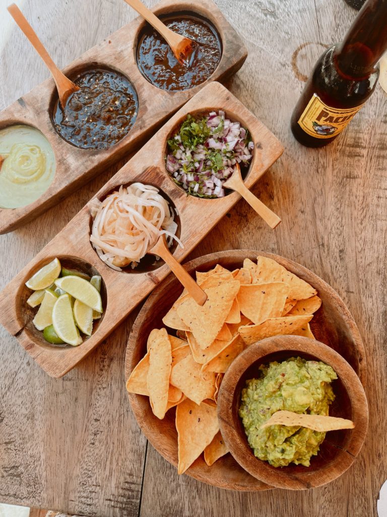 Guacamole and tortilla chips, with sides and a beer on a table.