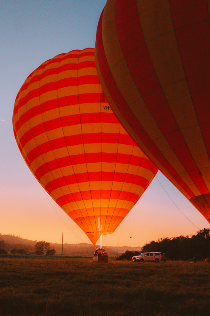 A orange hot air balloon firing up at dusk in a paddock next to a white truck