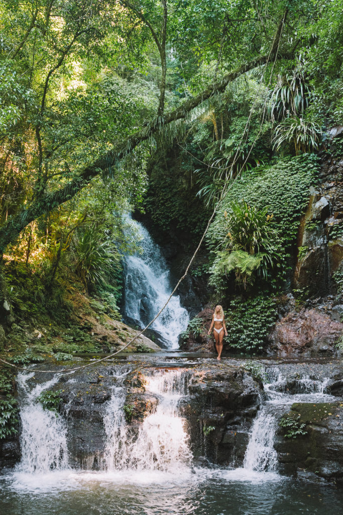 Woman walking on rocks of cascading waterfalls surrounded by lush green plants on the Gold Coast of Australia