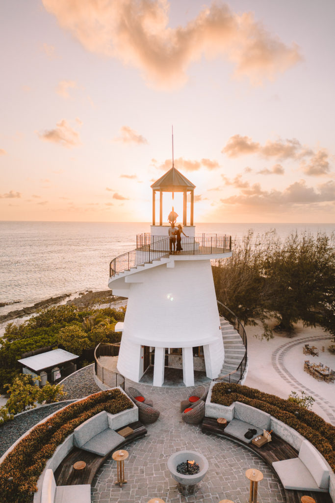 Couple standing together at top of lighthouse at sunset.