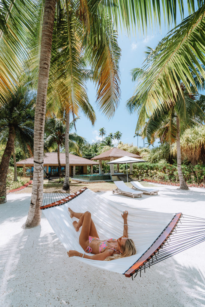 Woman laying in hammock that is suspended between palm trees.
