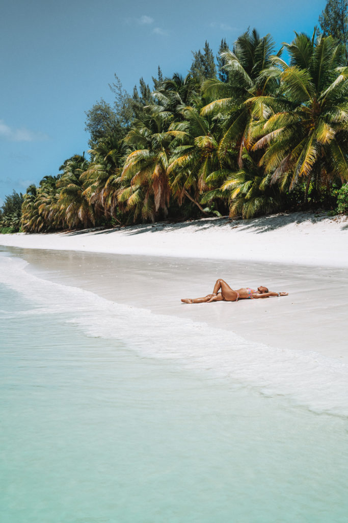 Woman laying in shallows of a palm tree lined beach.