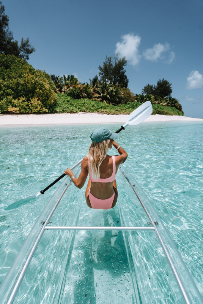 Woman paddling a glass bottom kayak in clear waters.