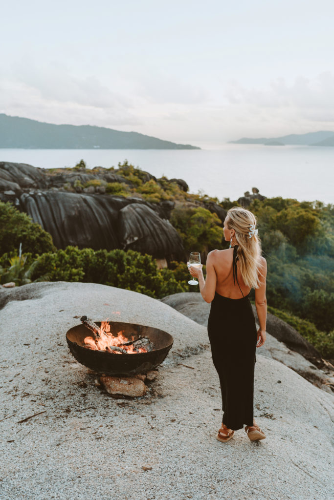 Woman holding glass of wine next to a fire pit at sunset, overlooking Felicite Island.