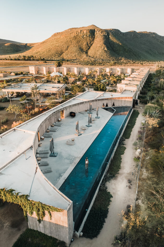 Woman walks into a pool. Aerial view showing the pool, as well as the rest of the hotel Paradero and the mountains beyond.