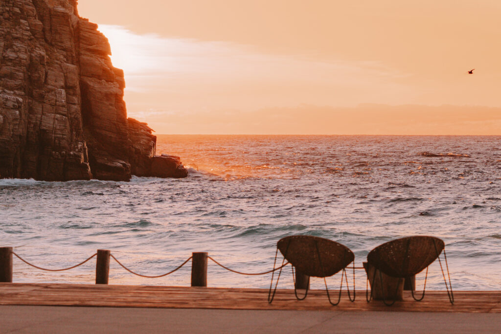 Two empty chairs facing the ocean with a golden setting sun over the ocean