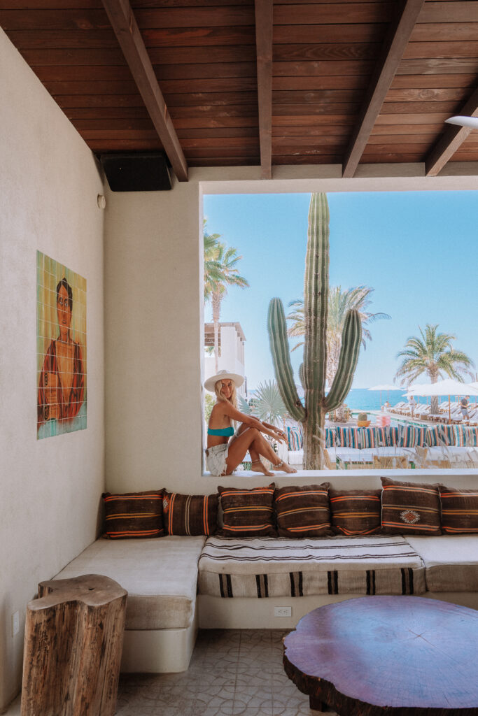 Woman sits in the window void at San Cristobal Hotel. There is a large cactus and colourful lounges in the foreground and background.
