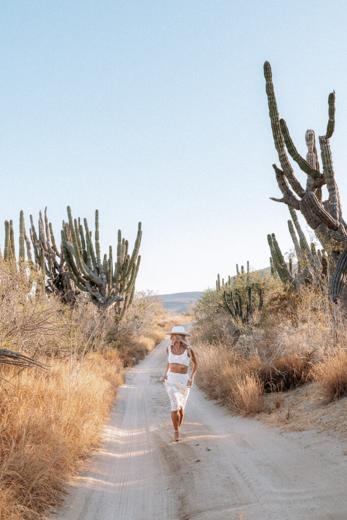 Woman runs on sandy path barefoot with cactus surrounding