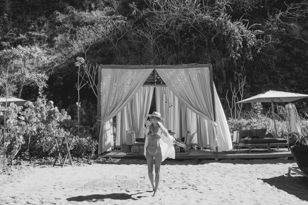 Black and what image of a woman at the beach with a cabana behind.