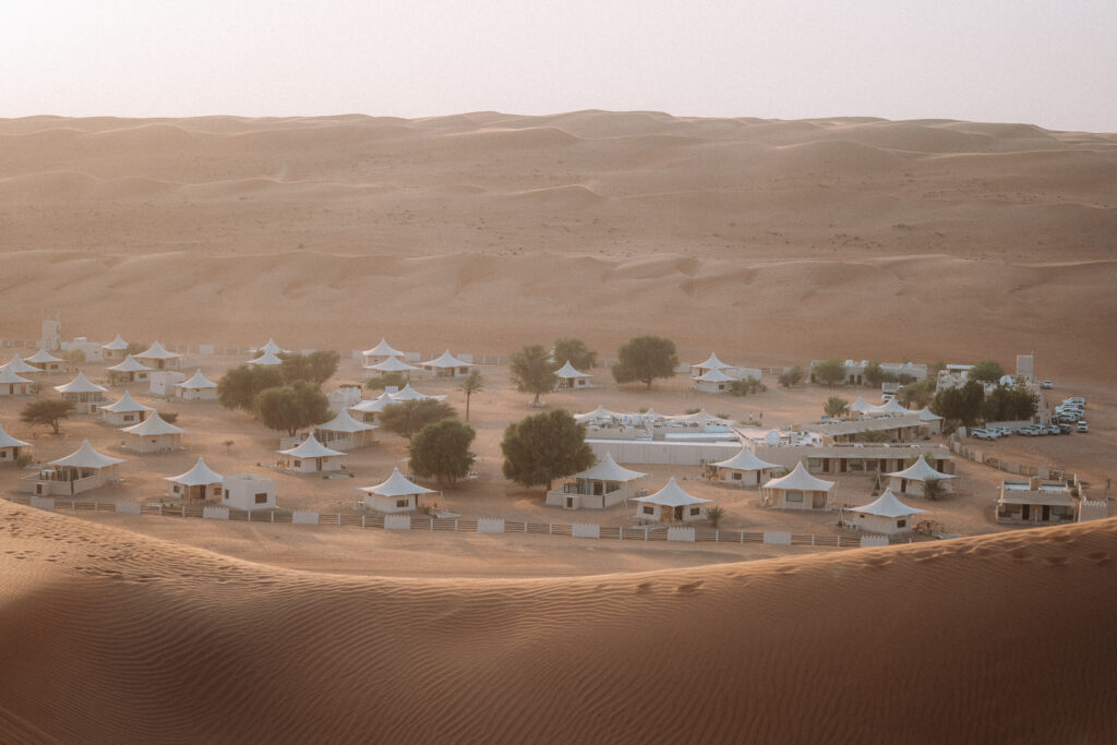 Desert Night Camp - scattered white canvas tents nestled together in between large sand dunes.