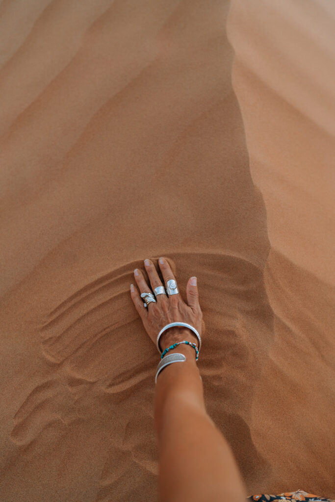 Close view of a womans hand pushing orange sand at her feet