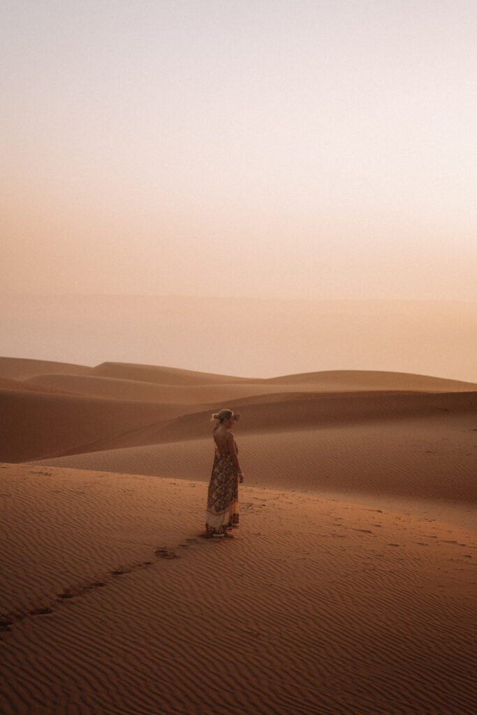 Woman covers eyes from setting sun in the orange sand dunes