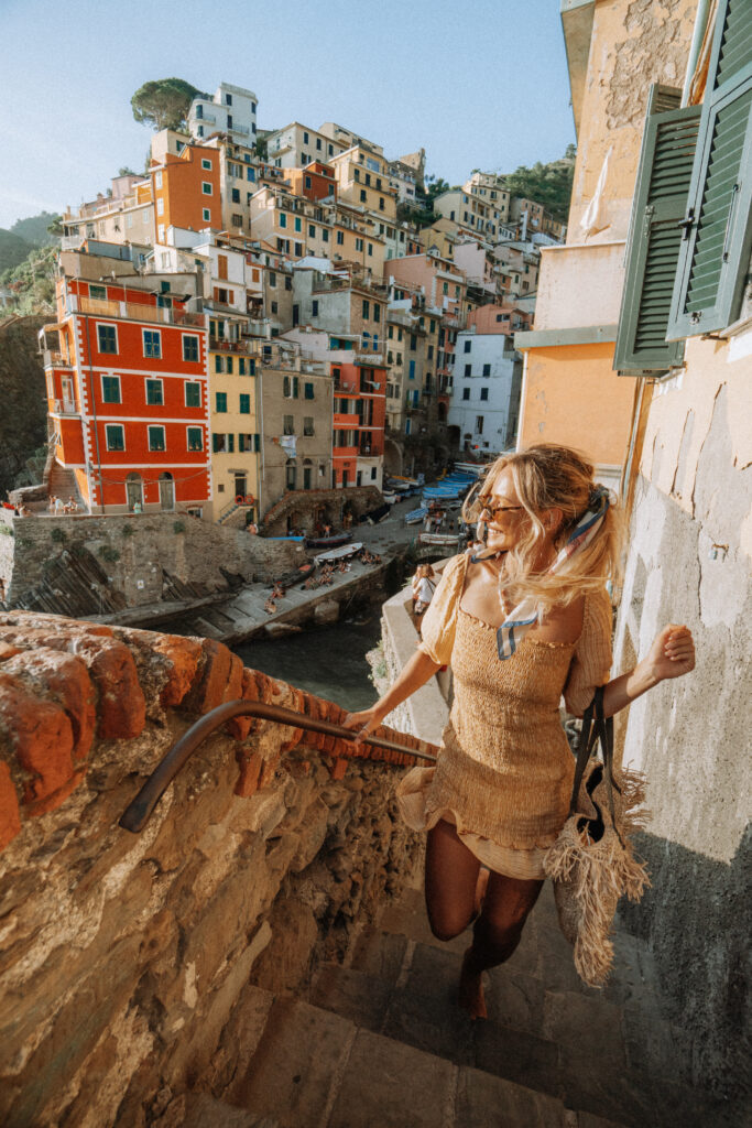 Woman walking up stairs with views of Riomaggiore village behind.