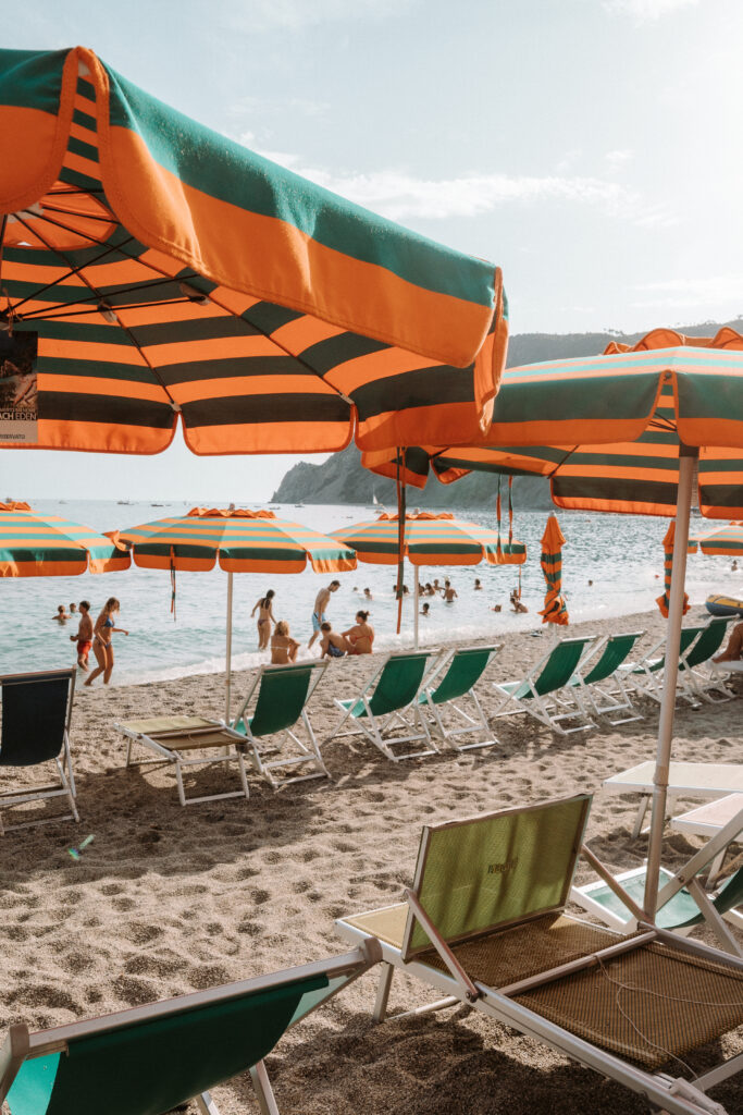 Beach umbrellas and chairs on the beach of Monterosso with the sea and people swimming behind.