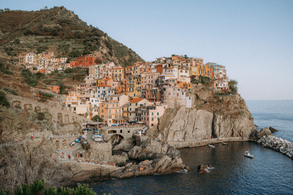 View of Manarola village, with coloured buildings on a clifftop and harbour below.