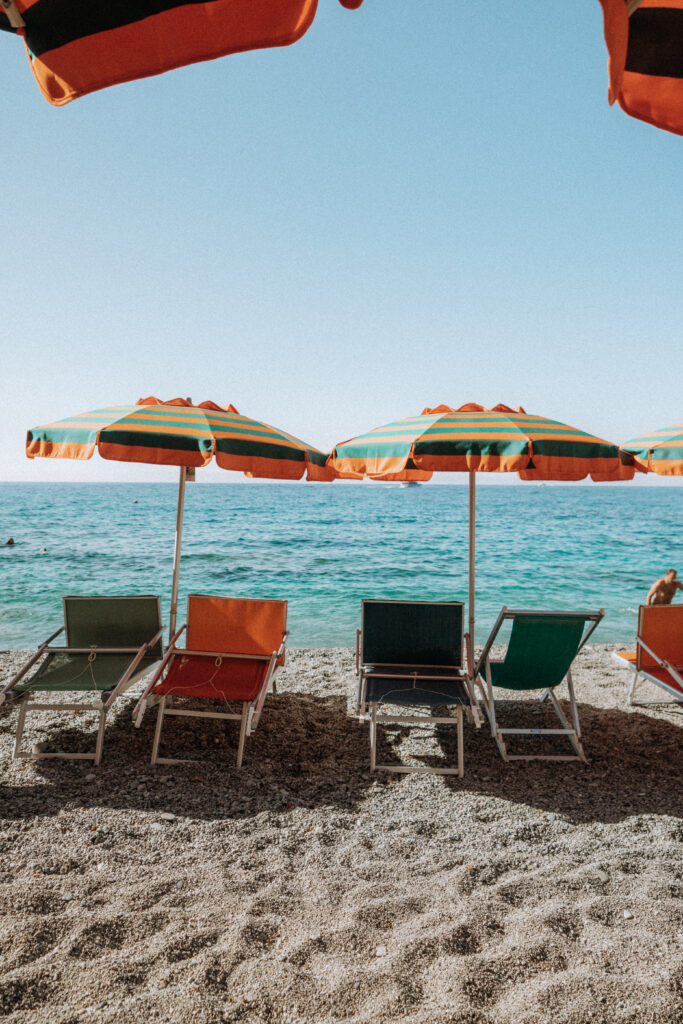 Beach umbrellas and chairs on the beach of Monterosso with the sea behind.