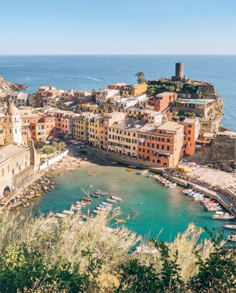 View from coastal hike above Vernazza, showing the harbour, beach and colourful buildings.