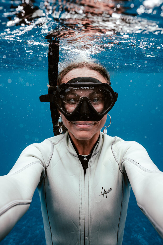Woman underwater with snorkelling mask on, smiling at the camera.