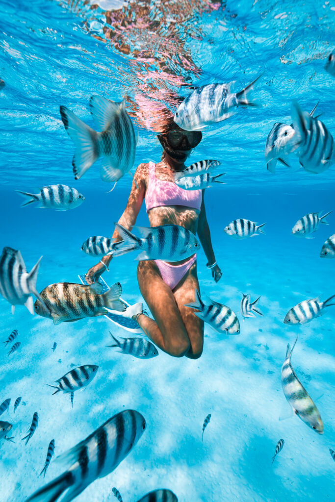 Woman swimming underwater, surrounded by plenty of black and white fish.