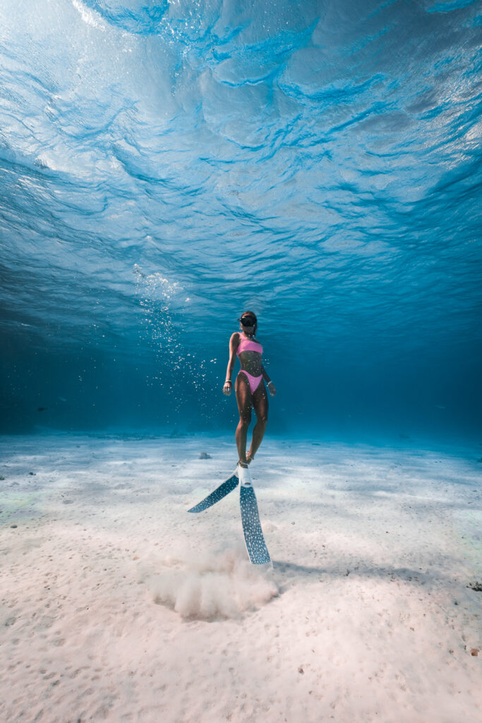 Woman free-diving in Bora Bora lagoon, with pink swim suit and long free-diving fins.