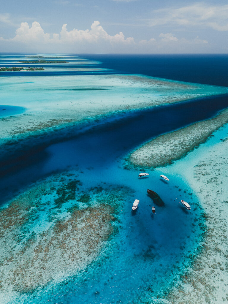 Aerial view of sunken shipwreck, surrounded by small speed boats, with coral reefs in the distance.