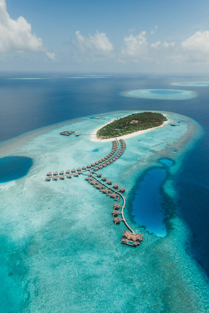 Aerial view of Vakkaru Resort island, with overwater villas spanning into the lagoon from the island.