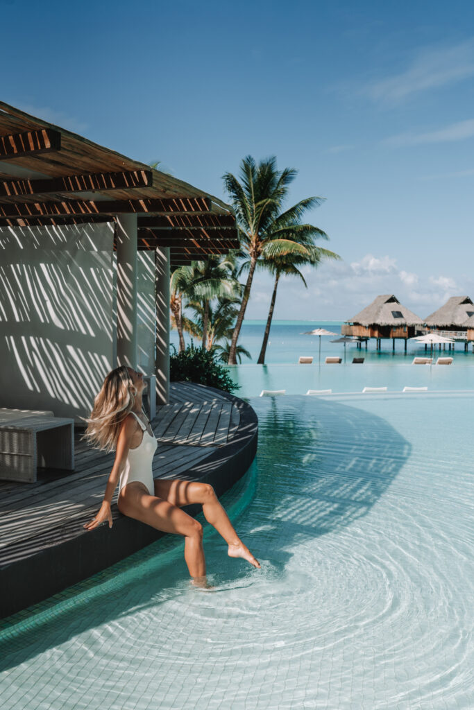 Woman sitting by the pool at a Bora Bora Resort with the turquoise water and overwater villas visible in the distance