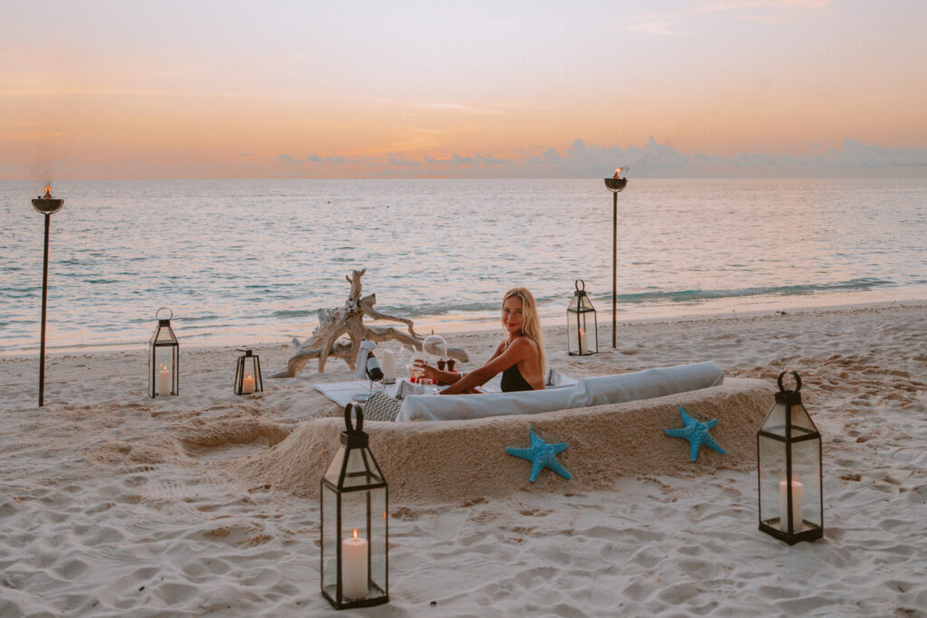 Woman sitting in sunken beach dinner with a glass of wine and candles surrounding her.