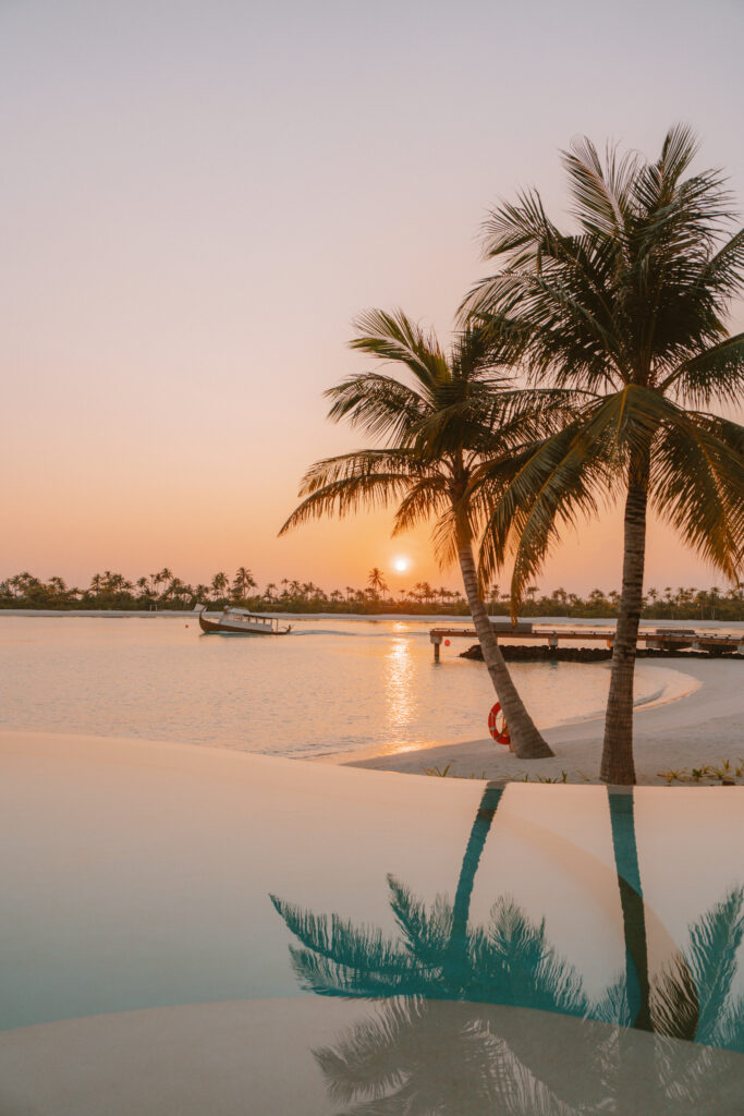 Sunset views of a pool, palms trees and a passing boat in the ocean.