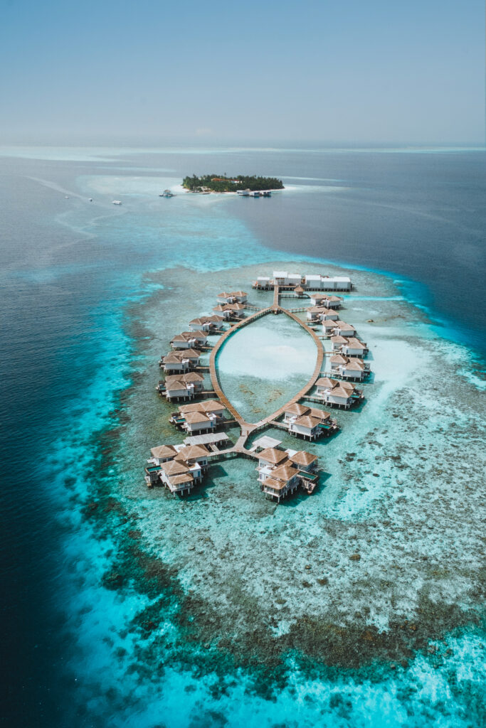 Aerial view of overwater villas at Raffles, with the island of Raffles in the background.