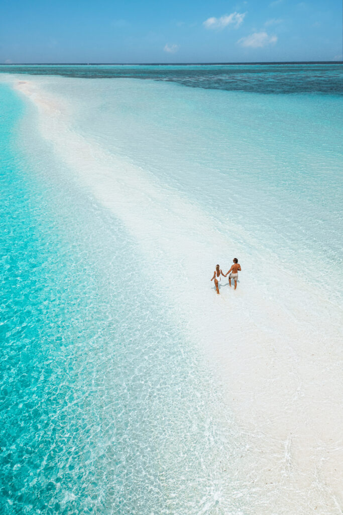 Couple holding hands and walking a long a sandbar.