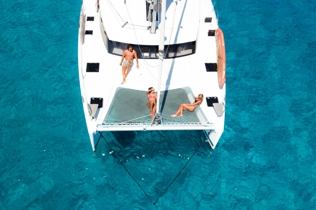 Three people laying on front deck of catamaran 