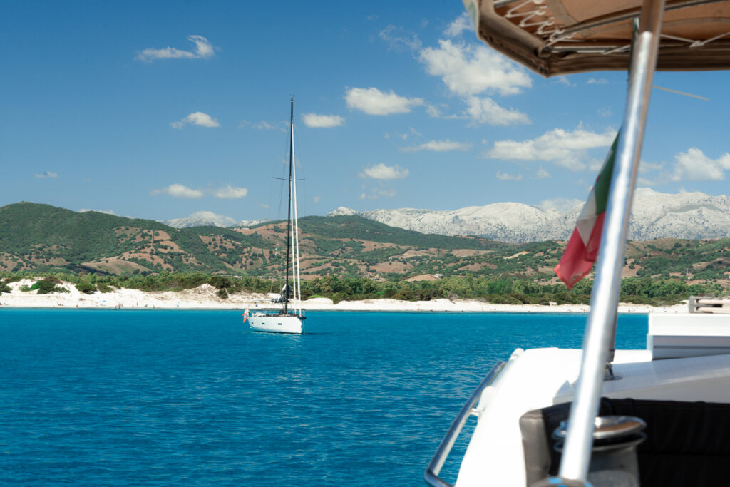 View over Sardinian waters from a catamaran with Italian flag in foreground.