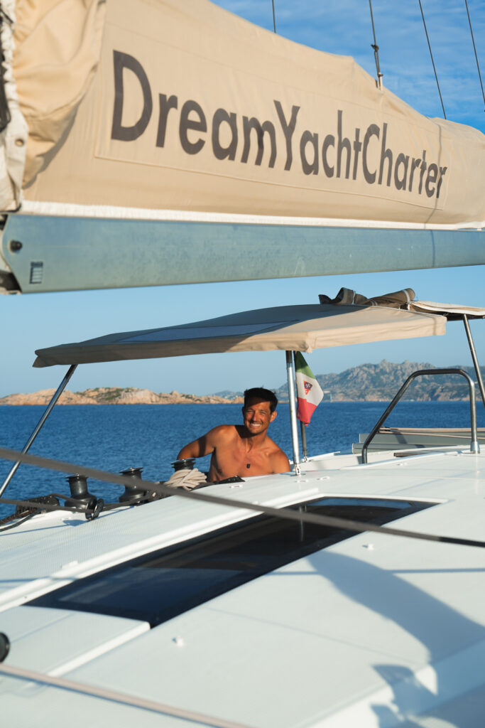 Skipper at the helm of catamaran, smiling at the camera