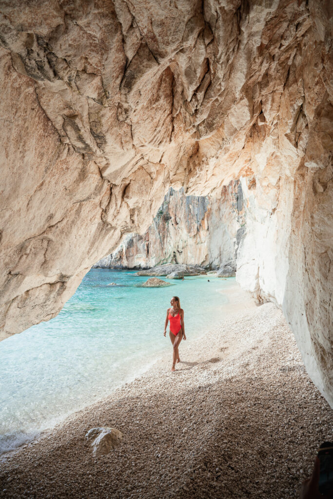 Woman walks into a cave on a pebble beach.