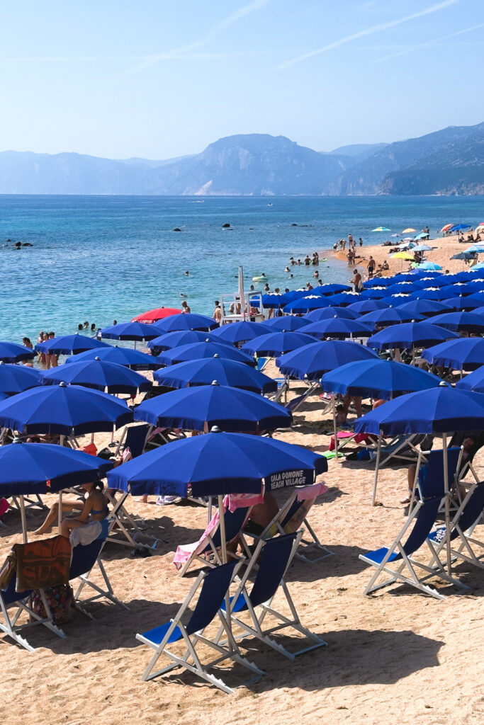 Blue beach umbrellas and bathers at a beach in Cala Gonome.