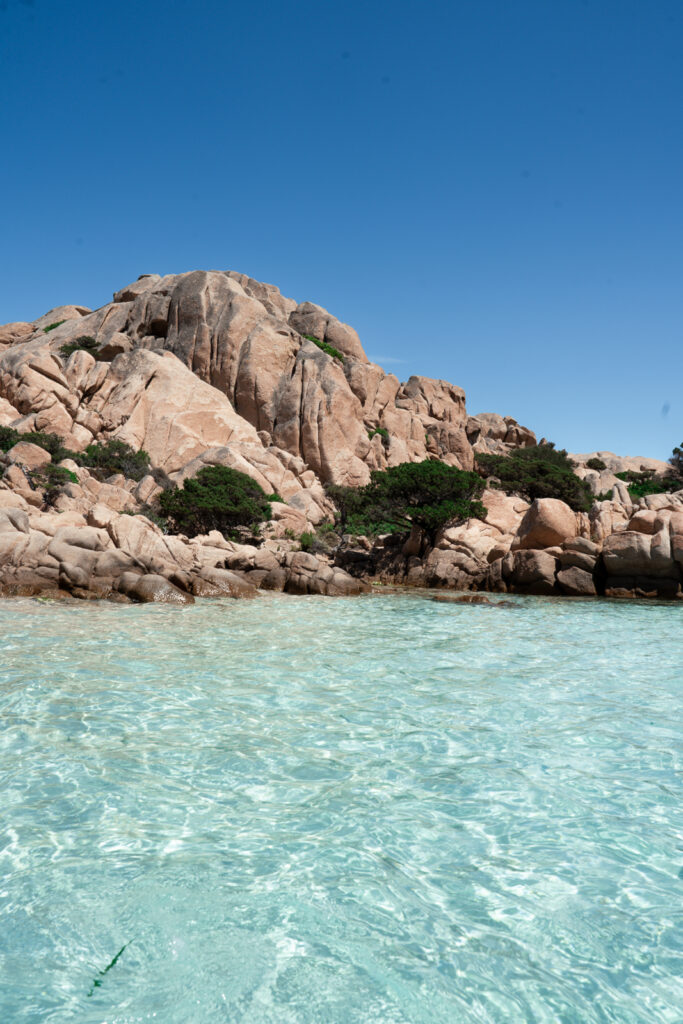 Cala Coticcio beach - blue water surrounded by rocky coastline.
