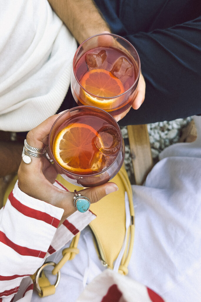 Two people's hands holding Negroni cocktails.