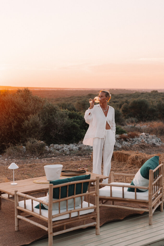 A woman drinking a glass of wine in a white suit at sunset at Morvedra Nou