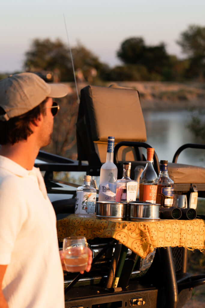 man holding a drink in front of a bar set up in the african bush