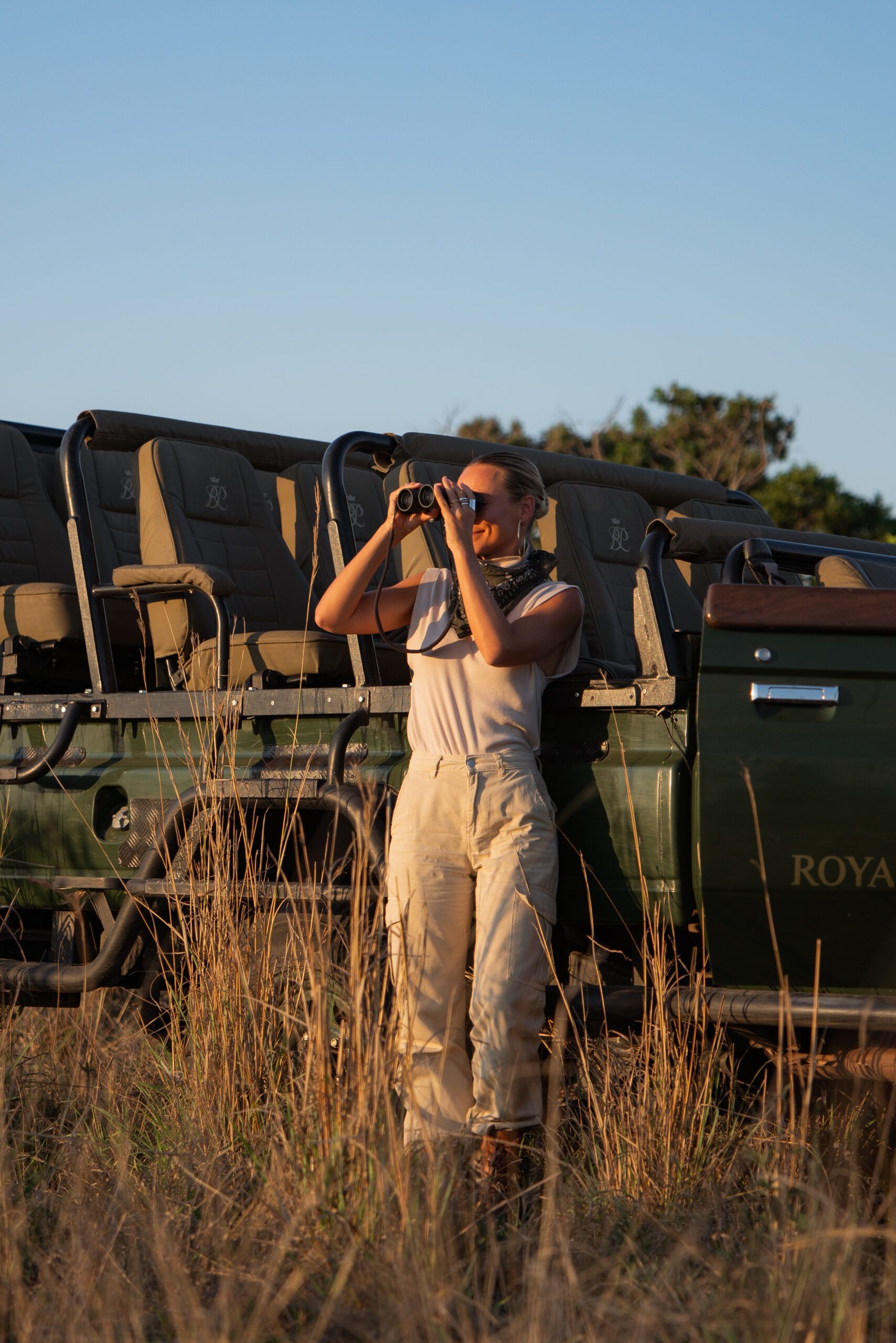 salty luxe using binoculars to look at wildlife in kruger national park while leaning on a royal malewane safari vehicle